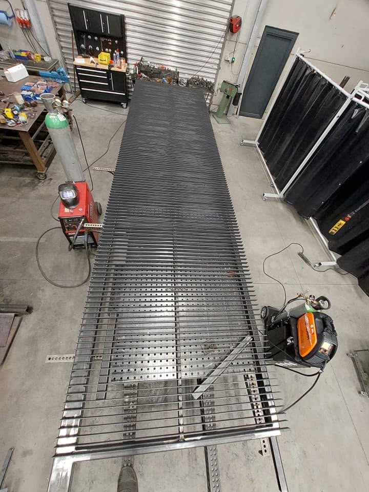 Lang stalen hekwerk in opbouw op de werktafel in het atelier