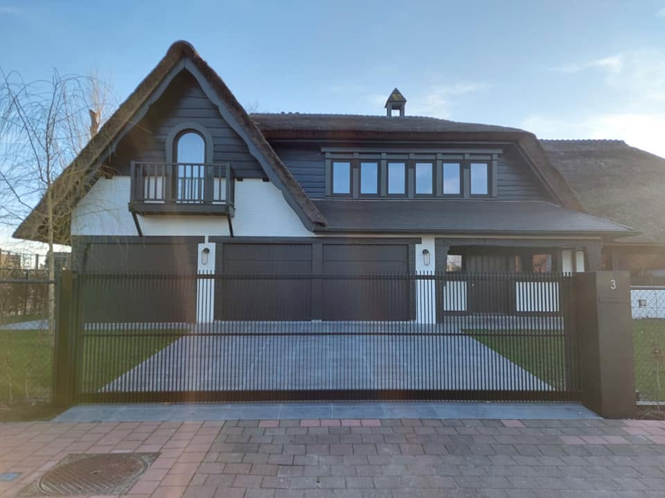Zwarte stalen poort voor een woning met rieten dak