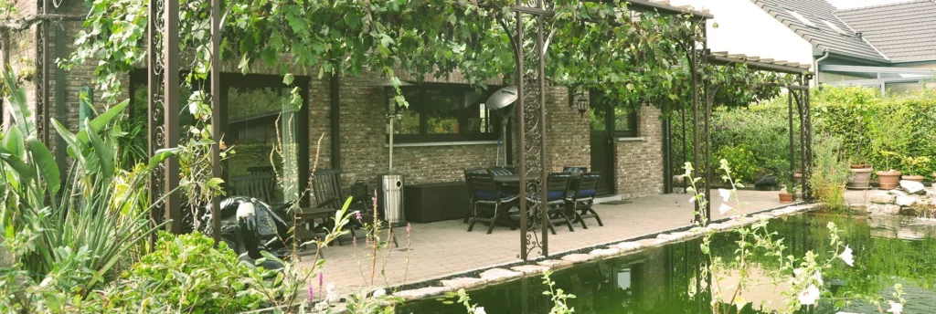 Pergola met smeedijzeren details boven een terras aan een vijver